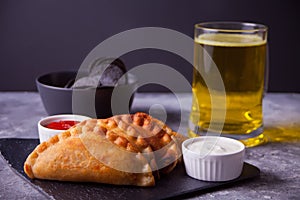 Mexican corn chips nachos, fried meat pies empanadas cheburek with dips and glass of beer. Black chips nachos for brutal men