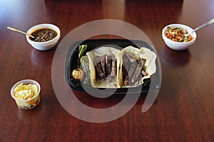 Mexican delicious beef tacos with roasted jalapeno and onion in a plastic container with salsas photo