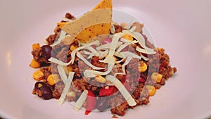 Mexican dish chili con carne lies on a pink plate with cheese and tortilla