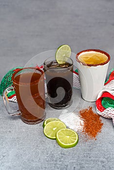 Mexican drinks Charro Negro, Jarrito, Cerveza roja on a gray table with salt pepper and lime photo