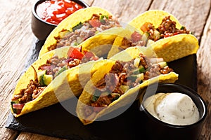 Mexican fast food tacos with chopped beef, cheese and vegetables served with sauces close-up on a slate boarde. horizontal