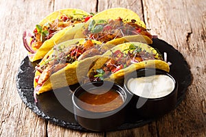 Mexican fast food tacos with glazed chicken, microgreen and vegetables served with sauces close-up on a slate boarde. horizontal