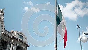 Mexican flag on flagpost and Palace of Fine Arts under beautiful blue sky