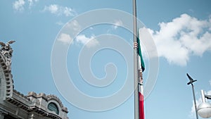 Mexican flag on flagpost and Palace of Fine Arts under beautiful blue sky