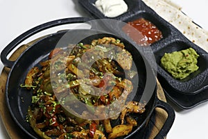 mexican food, chicken fajitas serving on a hot smoking sizzling plate with sour cream, guacamole, tomato salsa and tortilla bread