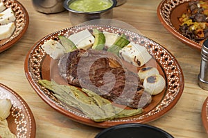 Mexican food, cut of meat served on a plate with nopal, avocado and onion on a wooden table photo