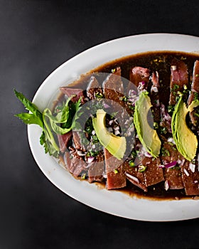 Mexican food, fish fajitas over a sauce, accompanied by avocado