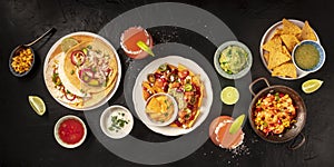 Mexican food, a flat lay panorama on a black background. Nachos, tortillas, Paloma cocktails, guacamole
