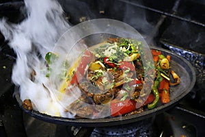 mexican food smoking chicken and beef fajitas on hot sizzling plate with fire and smoke