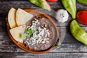 Mexican fried beans called Frijoles Refritos, plate of black beans on a wooden table in Mexico