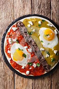 Mexican fried huevos divorciados eggs with salsa verde and roja, cheese, black beans on a tortilla close-up. Vertical top view photo