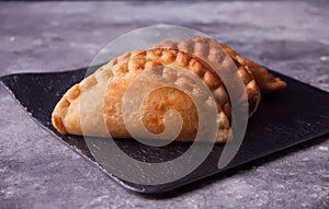 Mexican fried meat pies empanadas cheburek on the black plate on the concrete background