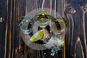 Mexican gold and silver tequila and lime salt on wood background