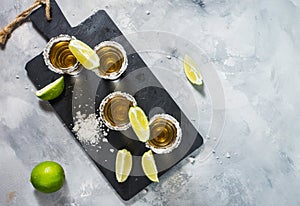 Mexican gold tequila with lime and salt on black stone background.