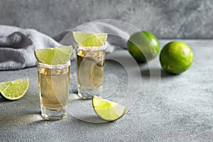 Mexican gold tequila in a shot glass, gray concrete background. Side view, selective focus