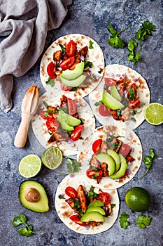 Mexican grilled chicken tacos with avocado, tomato, onion on rustic stone table. Recipe for Cinco de Mayo party.