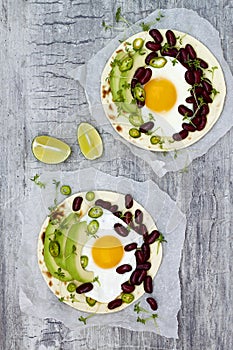 Mexican huevos rancheros tacos. Breakfast tostadas with black beans, avocado, fried egg, microgreens, sriracha ketchup. Top view photo