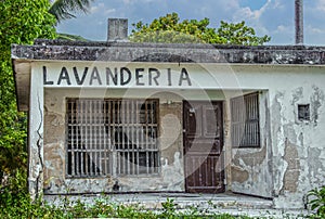 Mexican landromat or Lavanderia in grungy old building with stucco falling off concrete blocks and wooden bars at windows - weeds photo