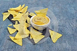 Mexican nachos chips with cheese sauce or dip in white bowl on black slate board