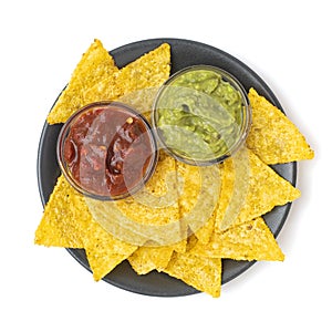 Mexican nachos tortilla chips with guacamole and salsa in dark plate. Isolated on white background. Top view