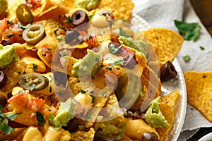 Mexican nachos tortilla chips with olives, jalapeno, guacamole, tomatoes salsa and cheese dip. close up