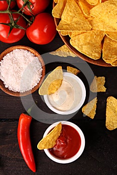 Mexican nachos in Wooden Bowl tortilla chips with chilli sauce, salsa and cheese dip, top view and Black Background