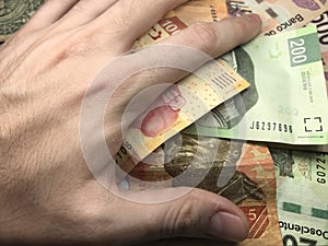 Mexican peso bills spread randomly over a flat surface with a hand over them