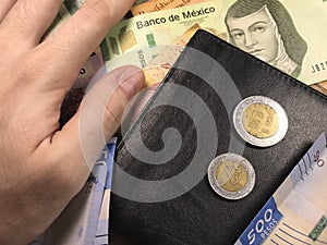 Mexican peso bills spread randomly over a flat surface with a hand over them