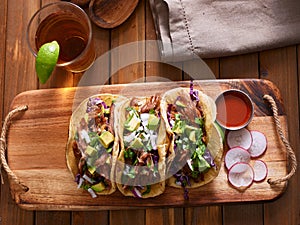 Mexican pork carnitas tacos with beer on wooden tray and radish garnish