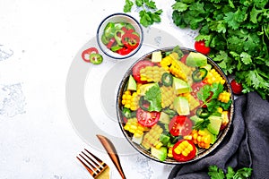 Mexican salad with sweet corn, avocado, jalapeno pepper, red tomatoes, cilantro and olive oil. White table background, top view
