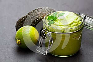 Mexican sauce guacamole in a jar on black stone background