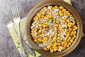 Mexican street corn snack Esquites with added sauce, chili, onion and cheese close-up in a plate on the table. Horizontal top view