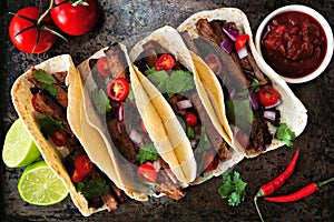 Mexican tacos with steak, tomatoes, onion and cilantro. Top on a dark background.