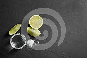 Mexican Tequila shot, lime slices and salt on black table. Space for text