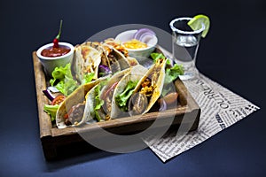 Mexican Tortilla with meat, beef and stewed vegetables and spicy sauce with a shot of tequila and lime on a wooden tray.