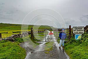 Mexican woman standing next to the gate where the coastal walk route starts from Doolin to the Cliffs of Moher