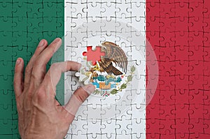 Mexico flag is depicted on a puzzle, which the man`s hand completes to fold