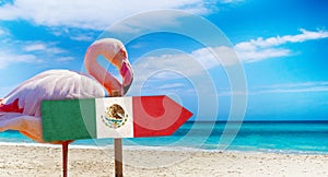 Mexico flag on wooden table sign on beach background with pink flamingo. There is beach and clear water of sea and blue sky in the