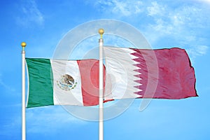 Mexico and Qatar two flags on flagpoles and blue cloudy sky