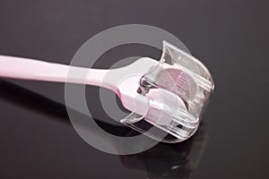 Mezoroller, dermaroller, mesotherapy skin tool. A mesoroller with a white handle and a pink rabbit on a dark mirror background. Ro