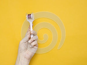 Mezoroller, dermaroller, mesotherapy skin tool in a woman`s hand on a yellow background. Copy space