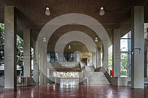 mezzanine, large empty room, brutalist architecture, with ceiling lamps, stairs and a red tile floor.