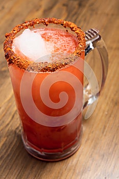 Michelada beer with tomato juice. Clamato with beer on wooden table. Mexican drink concept photo