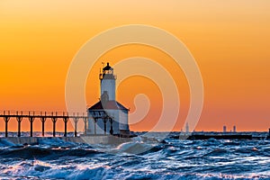 Michigan City, Indiana / USA : 03/23/2018 / Washington Park Lighthouse bathed in a beautiful sunset with Chicago looking over her