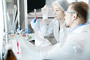 Microbiologists observing test glass with pink liquid