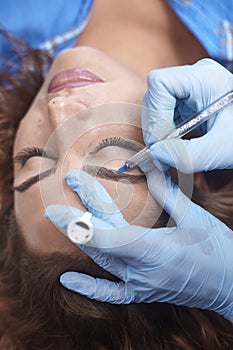 Microblading close-up, hands adding pigment to eyebrows, woman head face