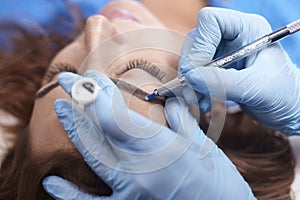 Microblading close-up, hands adding pigment to eyebrows, woman head face photo