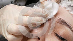 The microblading master wipes his eyebrows with a cotton pad and disinfects them, applies anesthesia. Microblading with