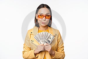 Microcredit and money concept. Stylish asian young woman in sunglasses, laughing happy, holding dollars cash, standing