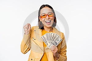 Microcredit and money concept. Stylish asian young woman in sunglasses, laughing happy, holding dollars cash, standing